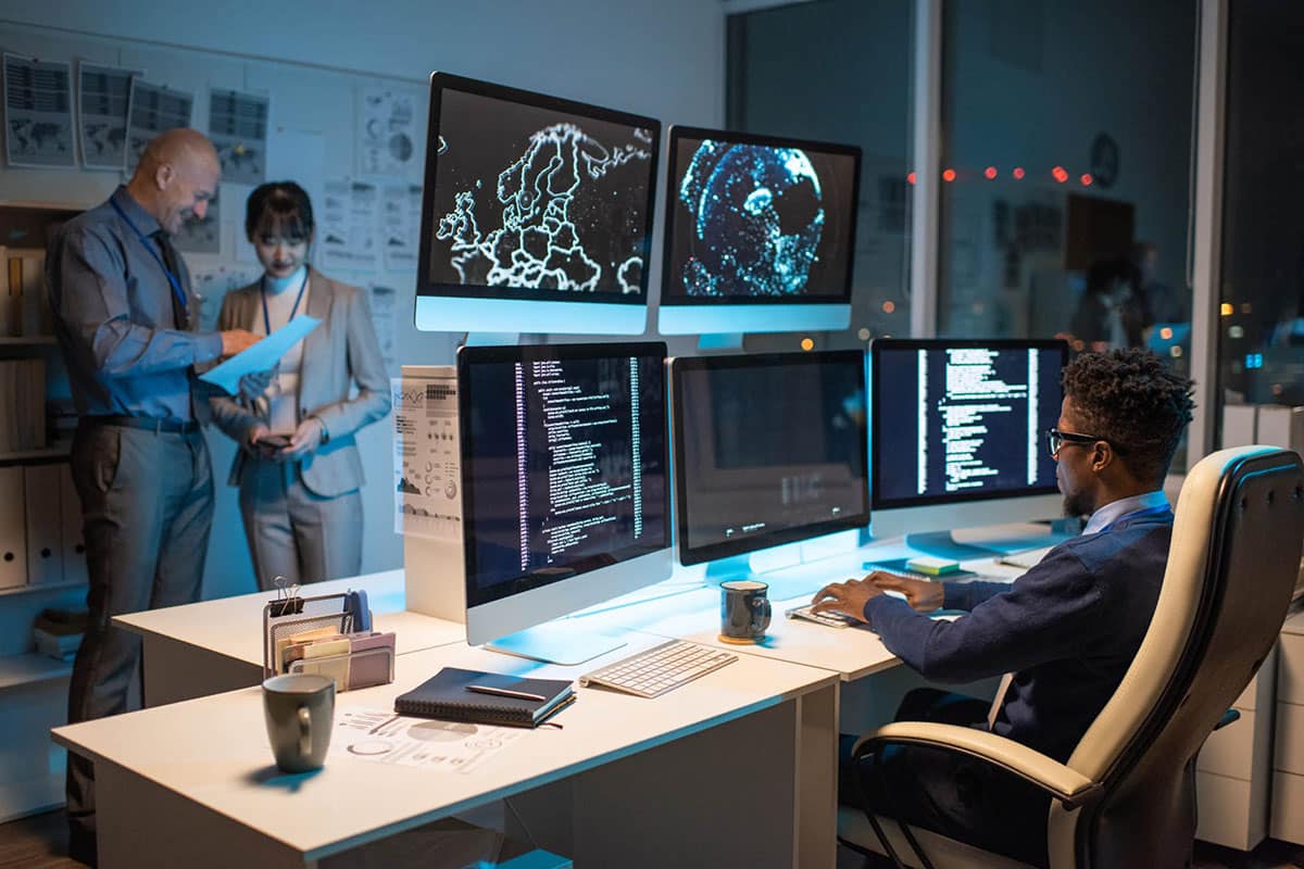 Person looking at data on computer screen while sitting in armchair in front of several monitors and typing.