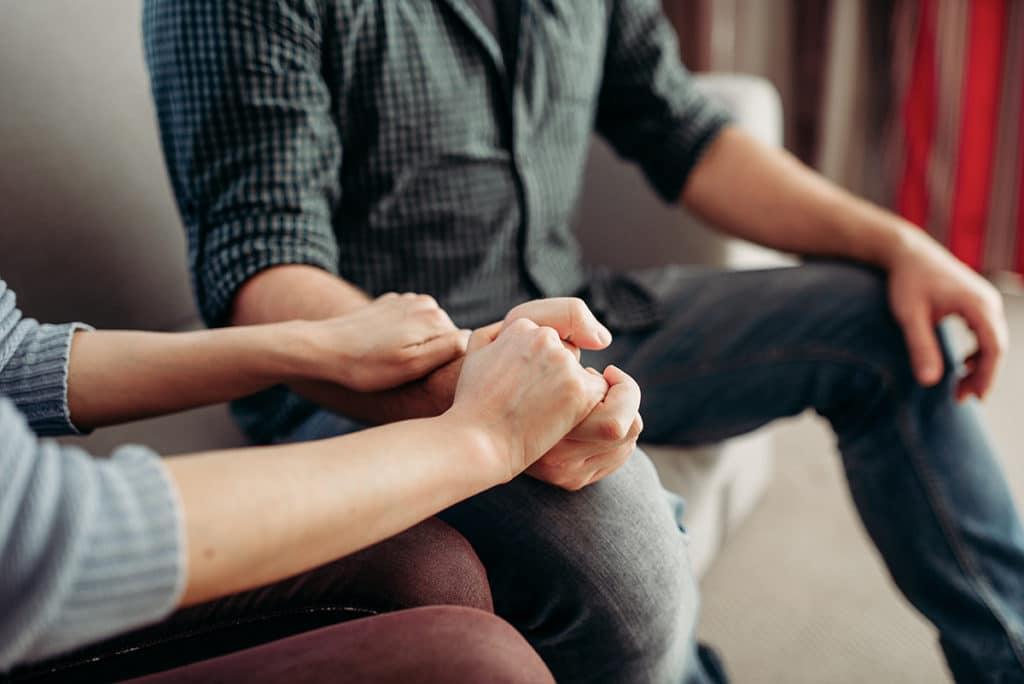 Two people comforting one another while sitting on couch.