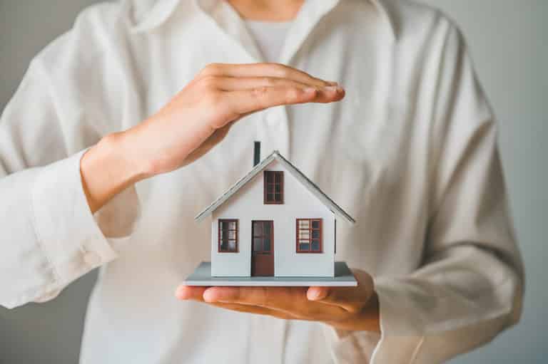 Hand protecting a small toy home to show the concept of home insurance.