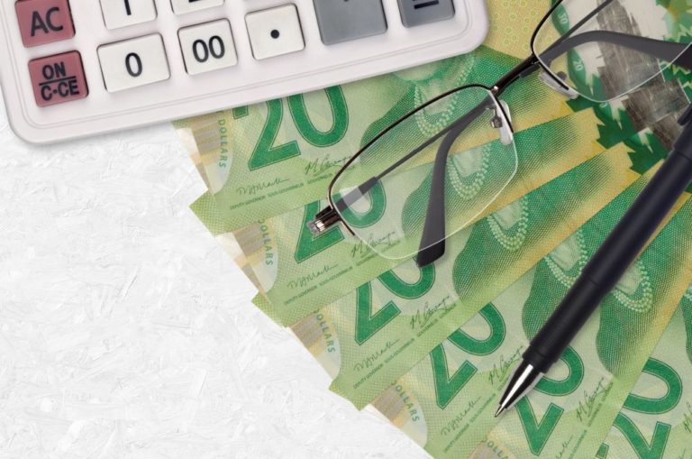 A calculator and prescription glasses sits atop a fan of money