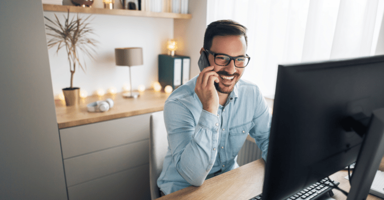 Person smiling while sitting at a desk and talking on phone.