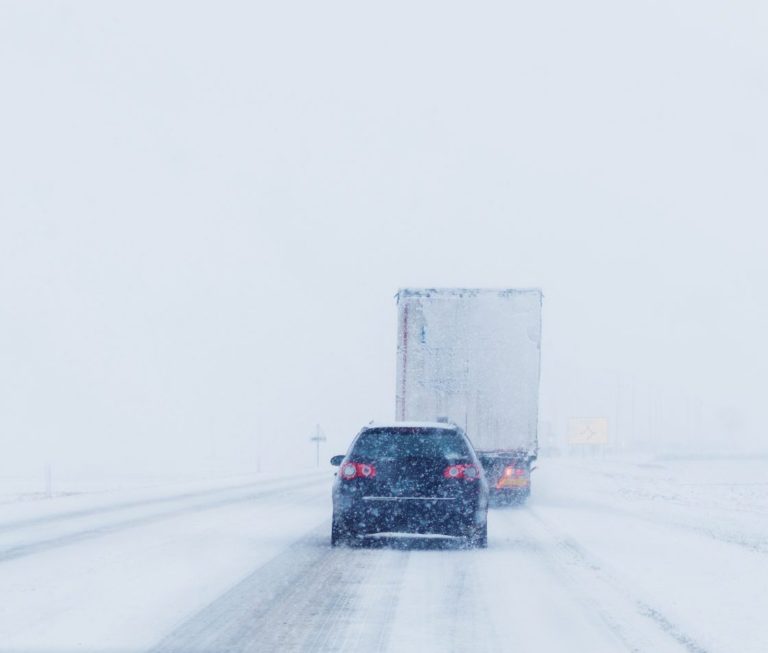 Vehicle travelling on snow-covered road in blizzard conditions.