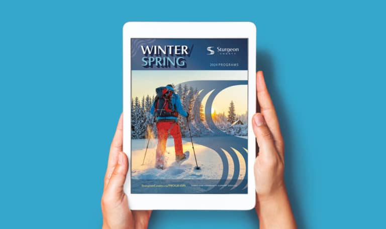 Two hands hold a tablet over a blue background. The tablet screen displays the cover page of a program guide.