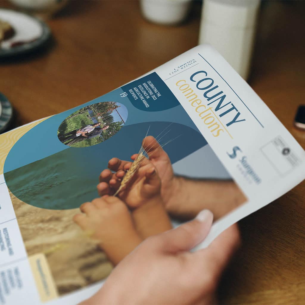 Close up of person hands holding a newsletter titled "County Connections" while sitting at a table.