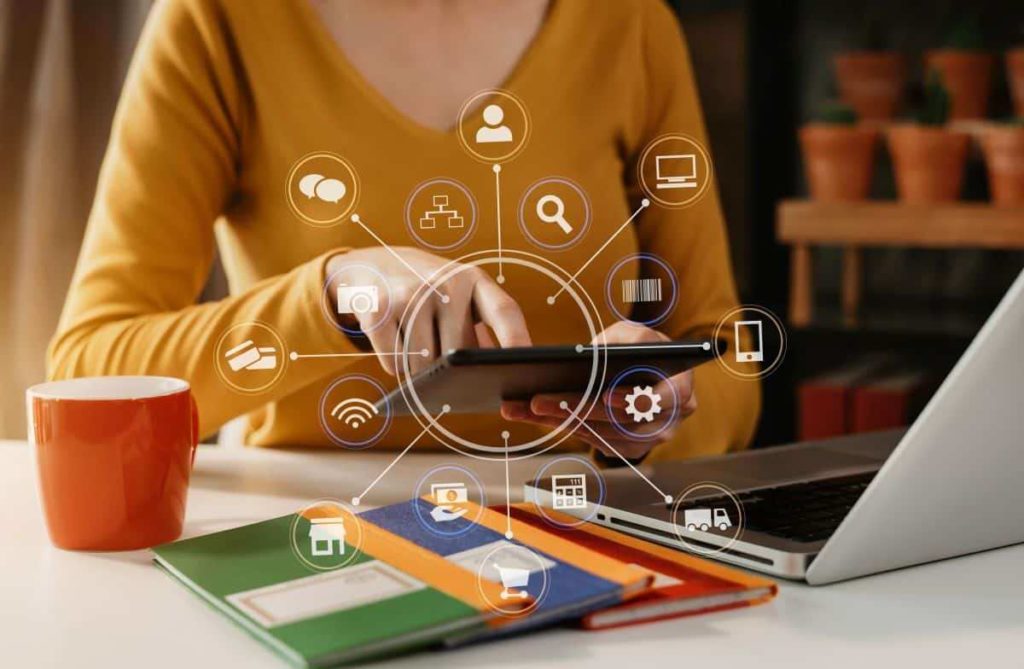 A person sits at a desk with a laptop, they are actively using a mobile phone. Various tech icons are overlaid.