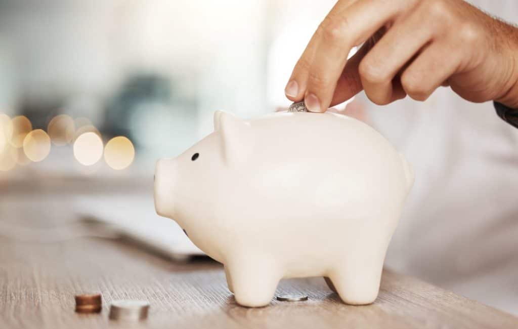 Hand places coins into a white piggy bank