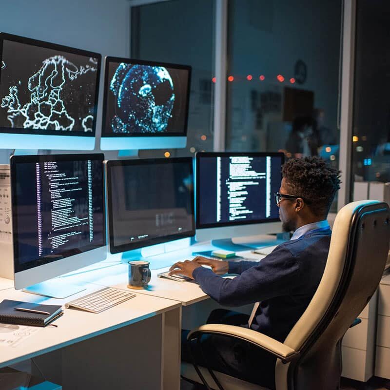 Person looking at data on computer screen while sitting in armchair in front of several monitors and typing.
